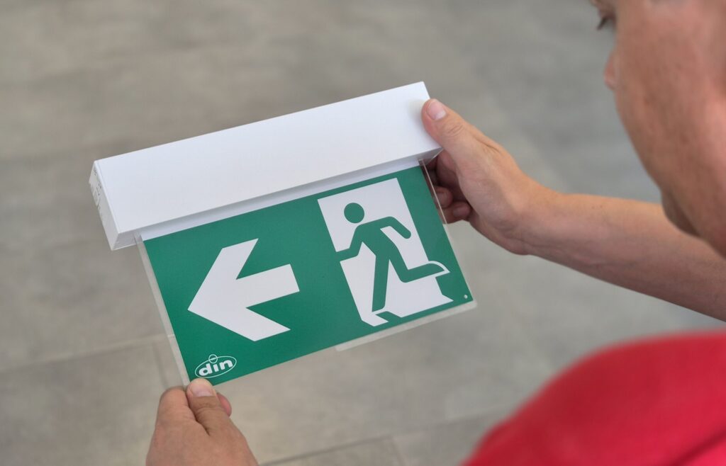Mitarbeiter hält Notausgangsschild in die Kamera.